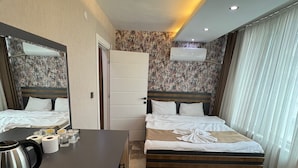 A hotel room with two beds, a desk with a kettle, a chair, and a bathroom door. - ELEGRAND HOTEL (Van)