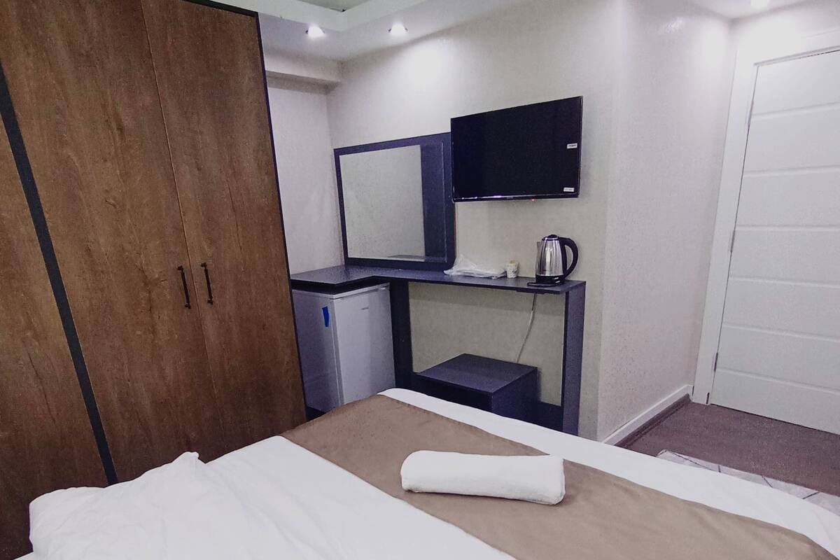 A hotel room with a bed, a desk, a mirror, a television, and a wardrobe.