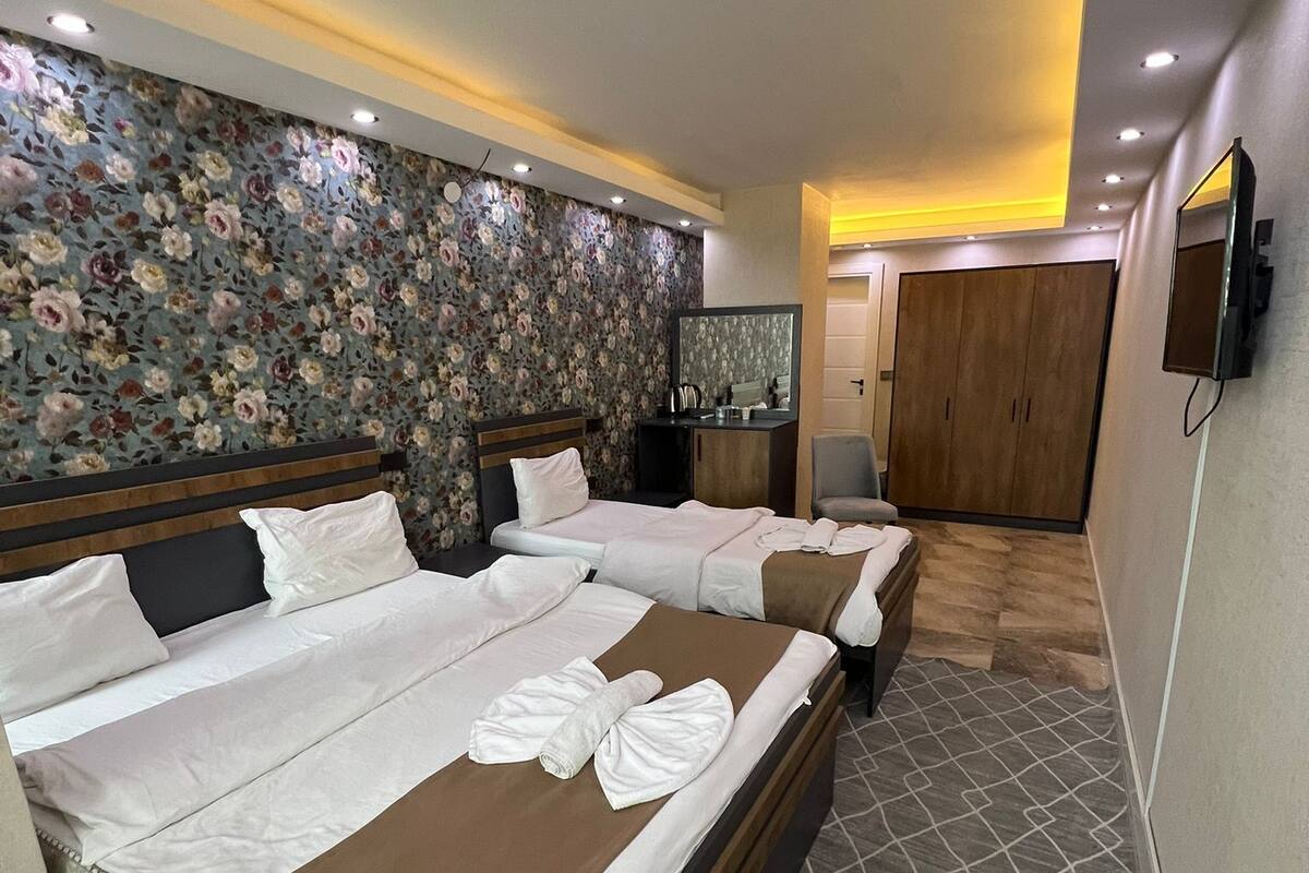 A hotel room with two beds, a wardrobe, a mirror, and a television.