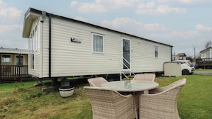 A mobile home with a patio area featuring wicker furniture and a small table. - Woodland Way (Pentraeth)
