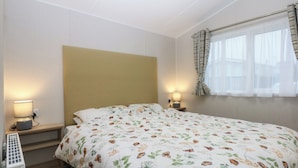 A hotel room with a bed, two bedside lamps, a heater, and a window with curtains. - Woodland Way (Pentraeth)