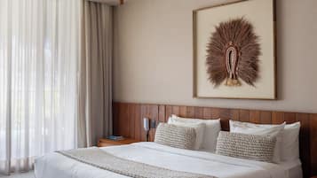 A hotel room with a large bed, wooden headboard, a framed artwork on the wall, and a nightstand with a lamp.