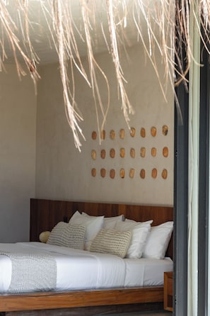 Een bed met een houten hoofdbord, witte beddengoed en een muur met ronde uitsparingen.