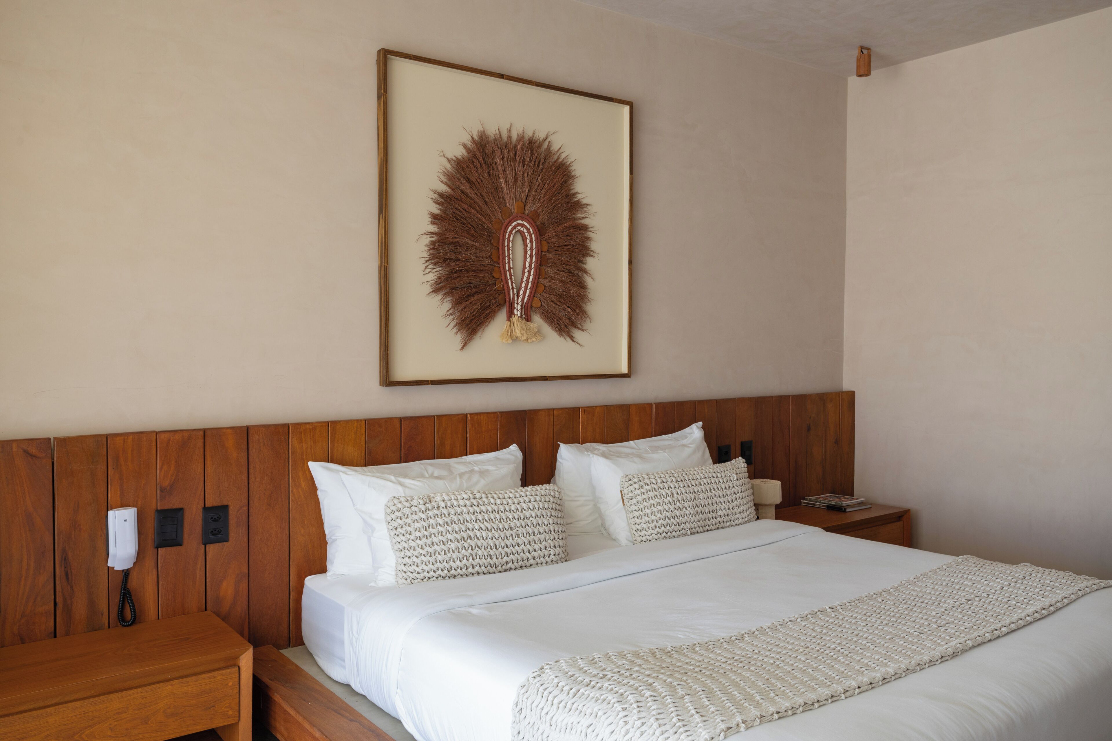 Quarto de hotel com cabeceira de madeira, cama com roupa de cama branca e uma obra de arte pendurada na parede.