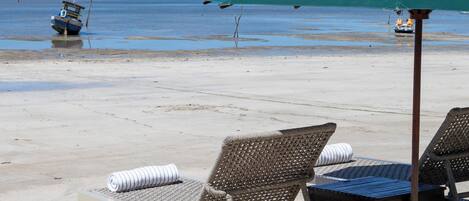 A beach with lounge chairs and a green umbrella, a boat in the water, and clear skies.