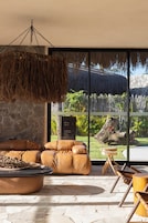 Un interior moderno con una pared de piedra, techo de paja colgante, sofá de cuero y vista a un paisaje tropical.