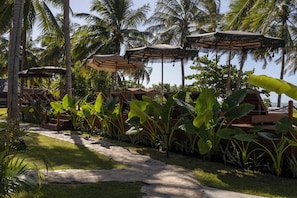 A tropical resort with thatched umbrellas, wooden lounge chairs, and lush greenery. - Evva Pousada (Porto de Pedras)