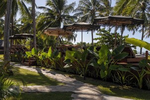 Un resort tropical con sombrillas de paja, sillones de madera y abundante vegetación.