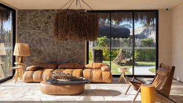 Una sala de estar moderna con pared de piedra, sofá de cuero y un ventanal con vistas a un paisaje tropical.