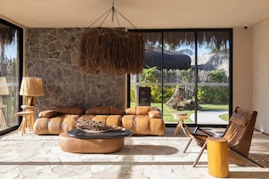 Una sala de estar moderna con pared de piedra, sofá de cuero y un ventanal con vistas a un paisaje tropical.