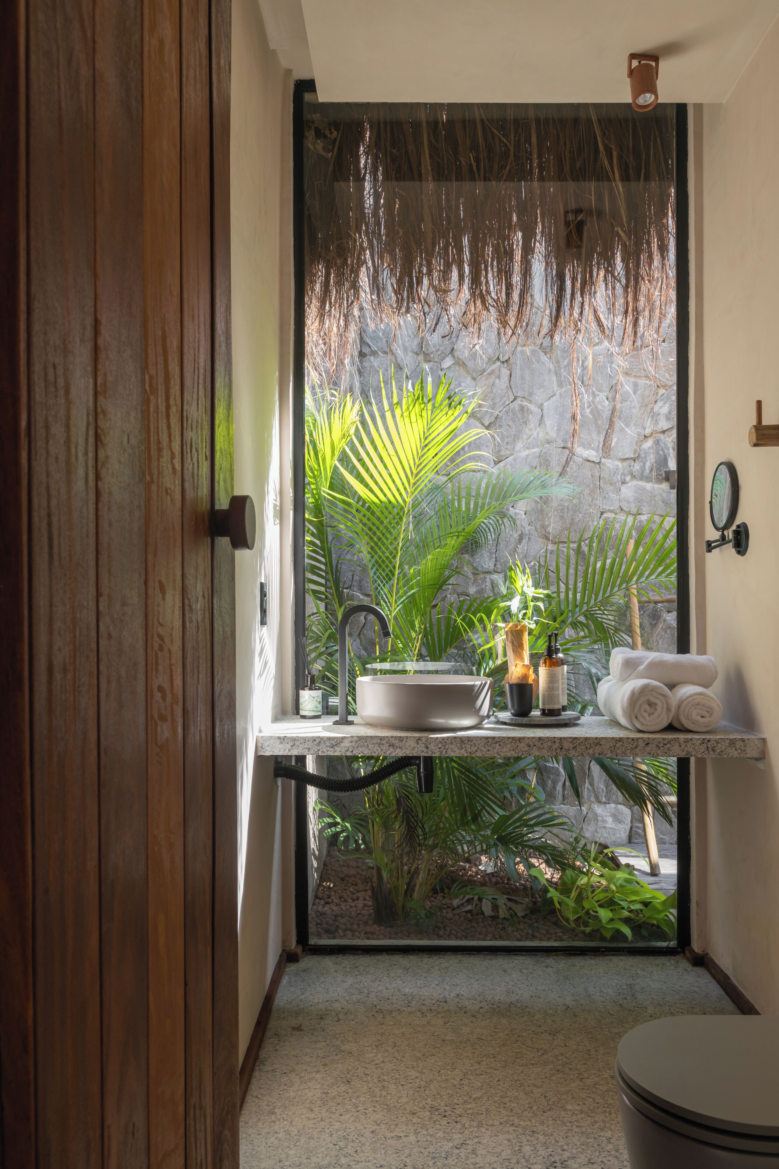 A bathroom with a stone wall, a sink, a mirror, and a toilet.