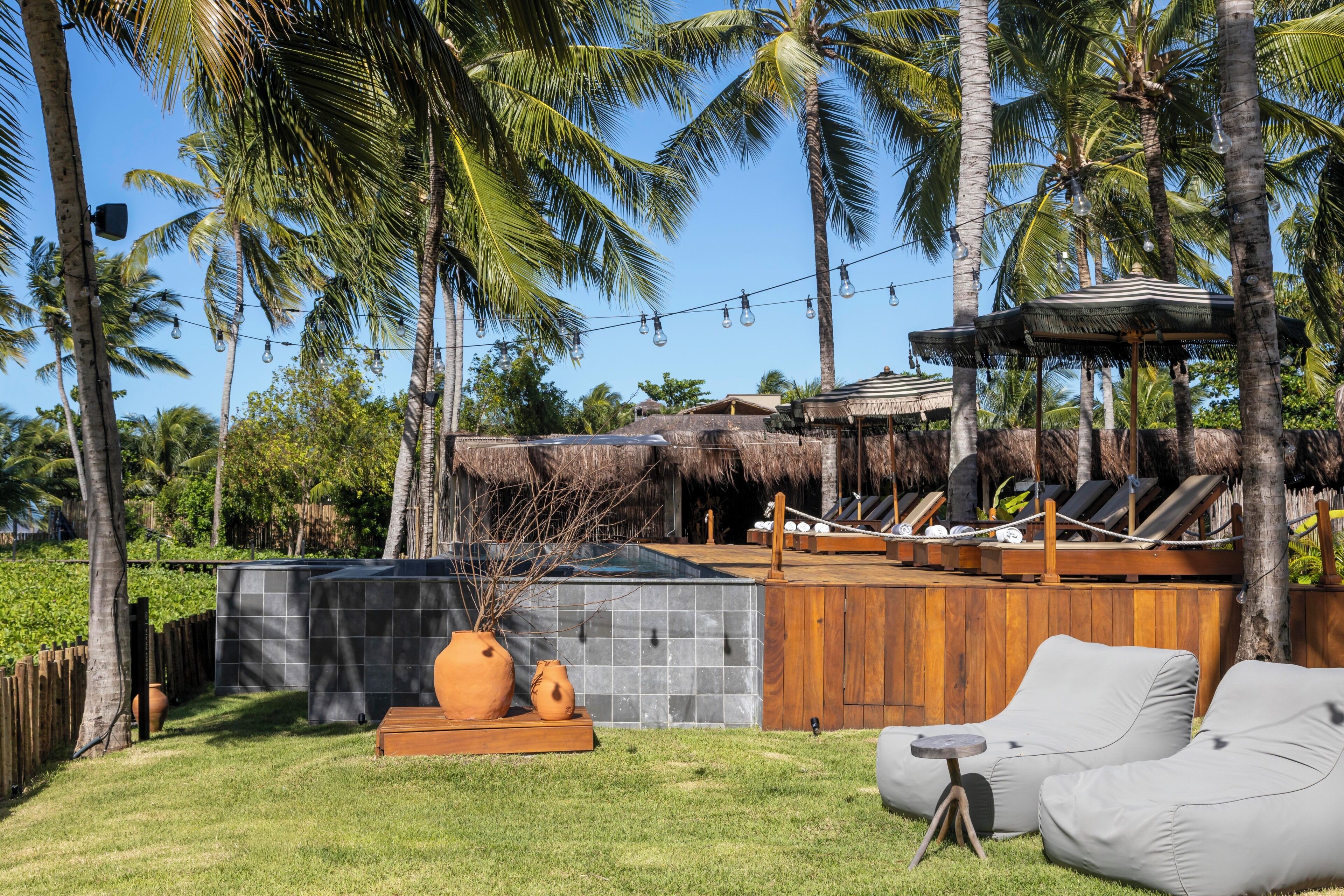 A tropical outdoor area with a pool, lounge chairs, and a thatched-roof structure.