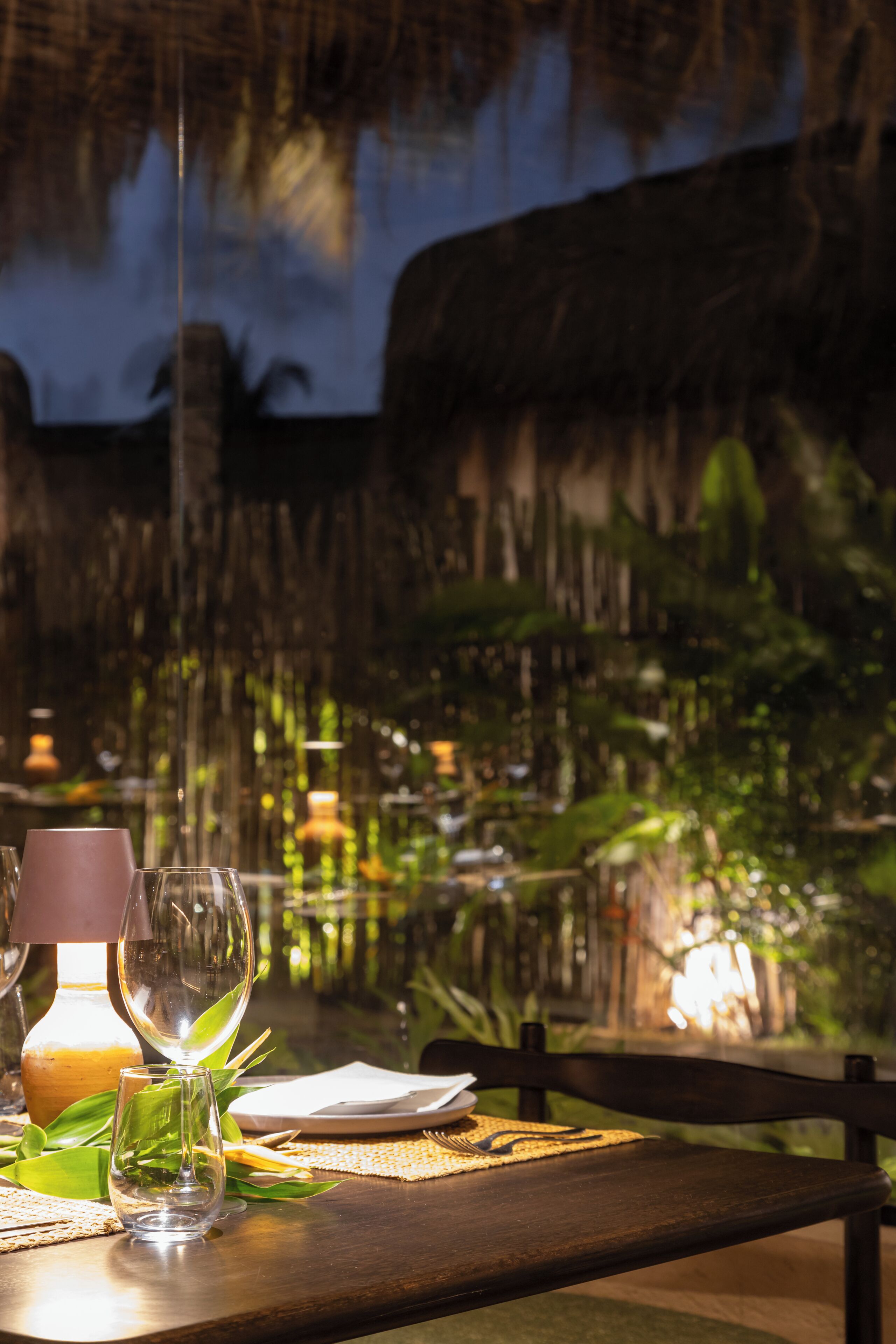 A dining table set with glasses and a bottle, with a tropical backdrop.