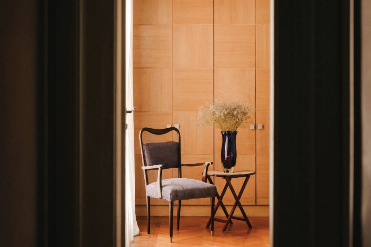 Une pièce avec un mur en bois, une chaise, une petite table et un vase contenant des fleurs séchées.