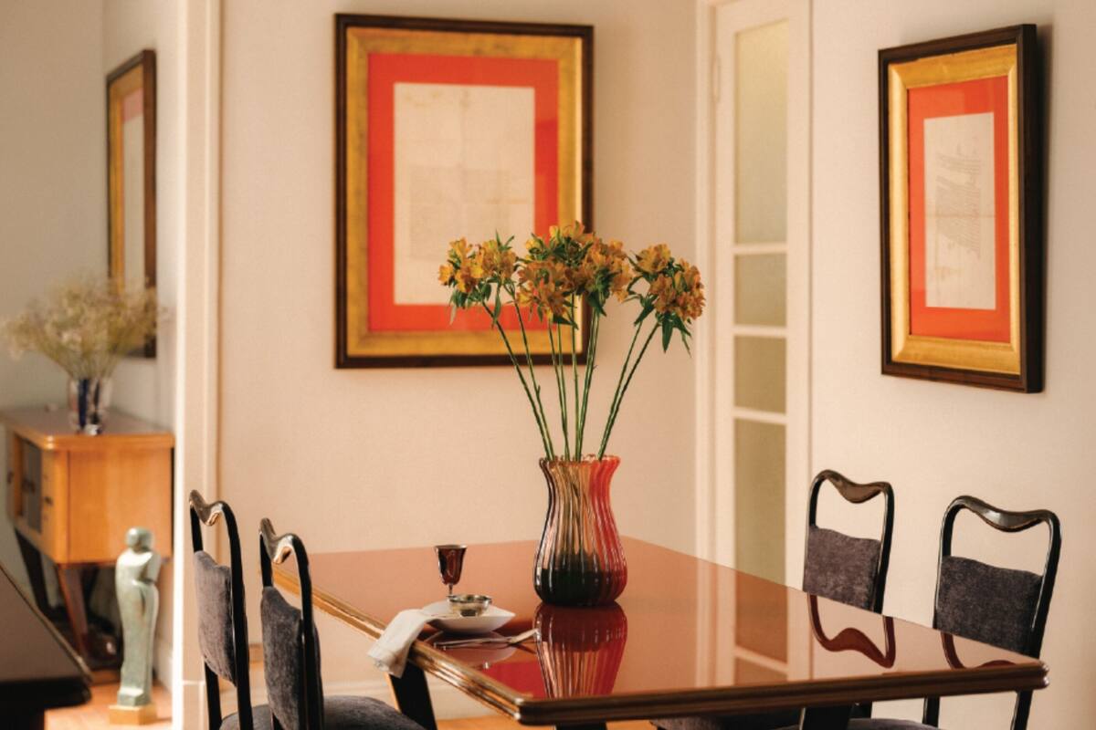 Una mesa de comedor con sillas, un jarrón con flores y cuadros en la pared.