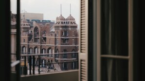Vista de un edificio histórico con múltiples arcos y cúpulas, visible a través de una ventana con persianas.