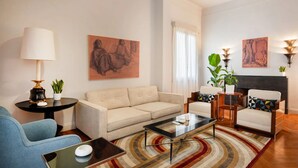 Una sala de estar con sofá, sillones, una mesa de centro, lámpara y obras de arte en las paredes.