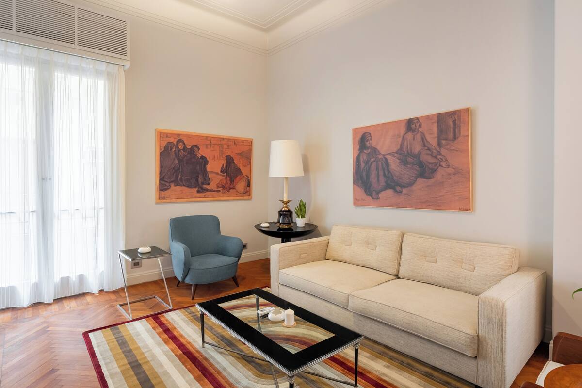 Una sala de estar con un sofá, un sillón azul, una mesa de centro y dos cuadros en la pared.