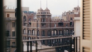 Vista de un edificio histórico con múltiples arcos y una torre central, vista a través de barrotes de ventana.