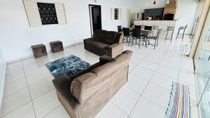 Ampla sala de estar com sofás, uma mesa de jantar com cadeiras e uma cozinha com forno de tijolos.