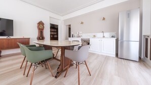 Eine moderne Küche mit Essbereich, weißen Schränken, einem großen Kühlschrank und einem Holztisch mit Stühlen.