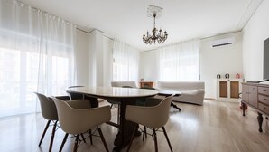 Ein modernes Wohnzimmer mit Esstisch, Stühlen, einer Couch, einer Pendelleuchte und einem Fernseher.