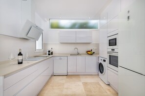 A modern kitchen with white cabinetry, a dishwasher, a washing machine, and a microwave. - Villa Deluxe Suites Maspalomas (Maspalomas)