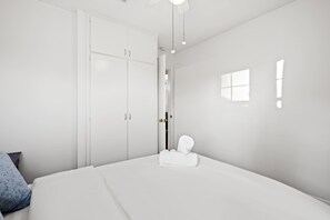 Ein schlicht eingerichtetes Schlafzimmer mit einem großen Bett, einem weißen Kleiderschrank und einem kleinen Fenster.