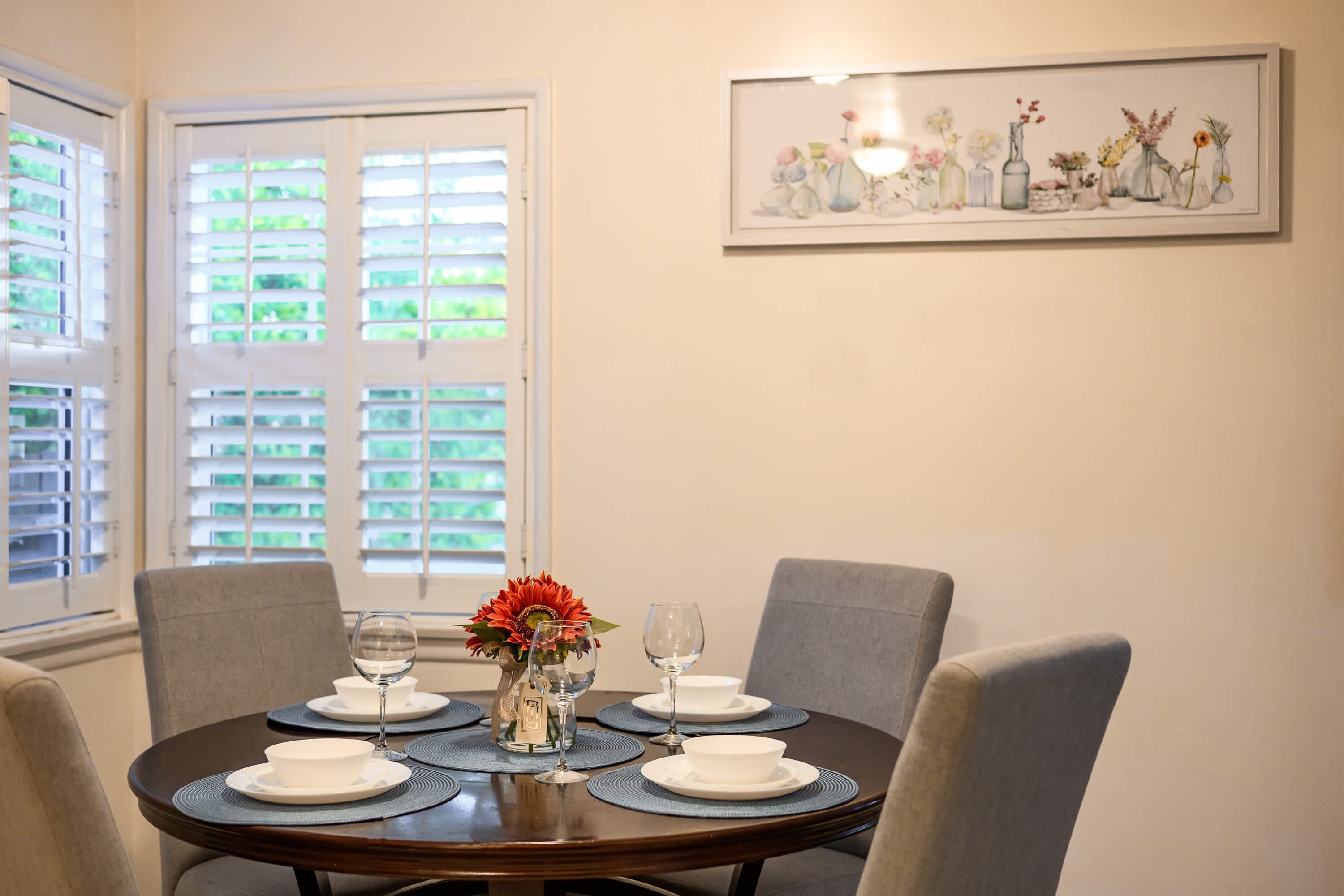 A dining table set with white plates, glasses, and a vase with flowers.