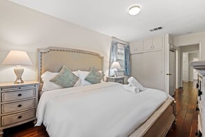 Ein ordentlich eingerichtetes Schlafzimmer mit einem großen Bett, Nachttischen, einem Kleiderschrank und einem durch eine offene Tür einsehbaren Badezimmer.