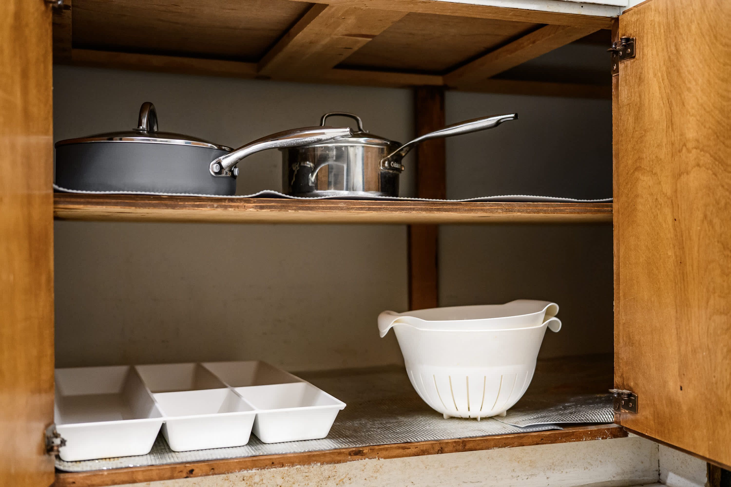 A kitchen with wooden shelves, a white colander, and a metal pot.