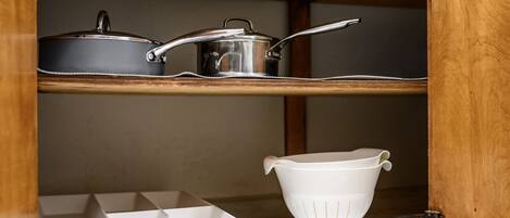 A kitchen with wooden shelves, a white colander, and a metal pot.