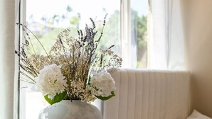 Ein Zimmer mit einem Bett, einem Vorhangfenster und einer Blumenvase auf einem Nachttisch.