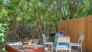 Eine Außenpatio-Terrasse mit Holztisch, zwei weißen Stühlen, einem kleinen Grill und einem Holzzaun.