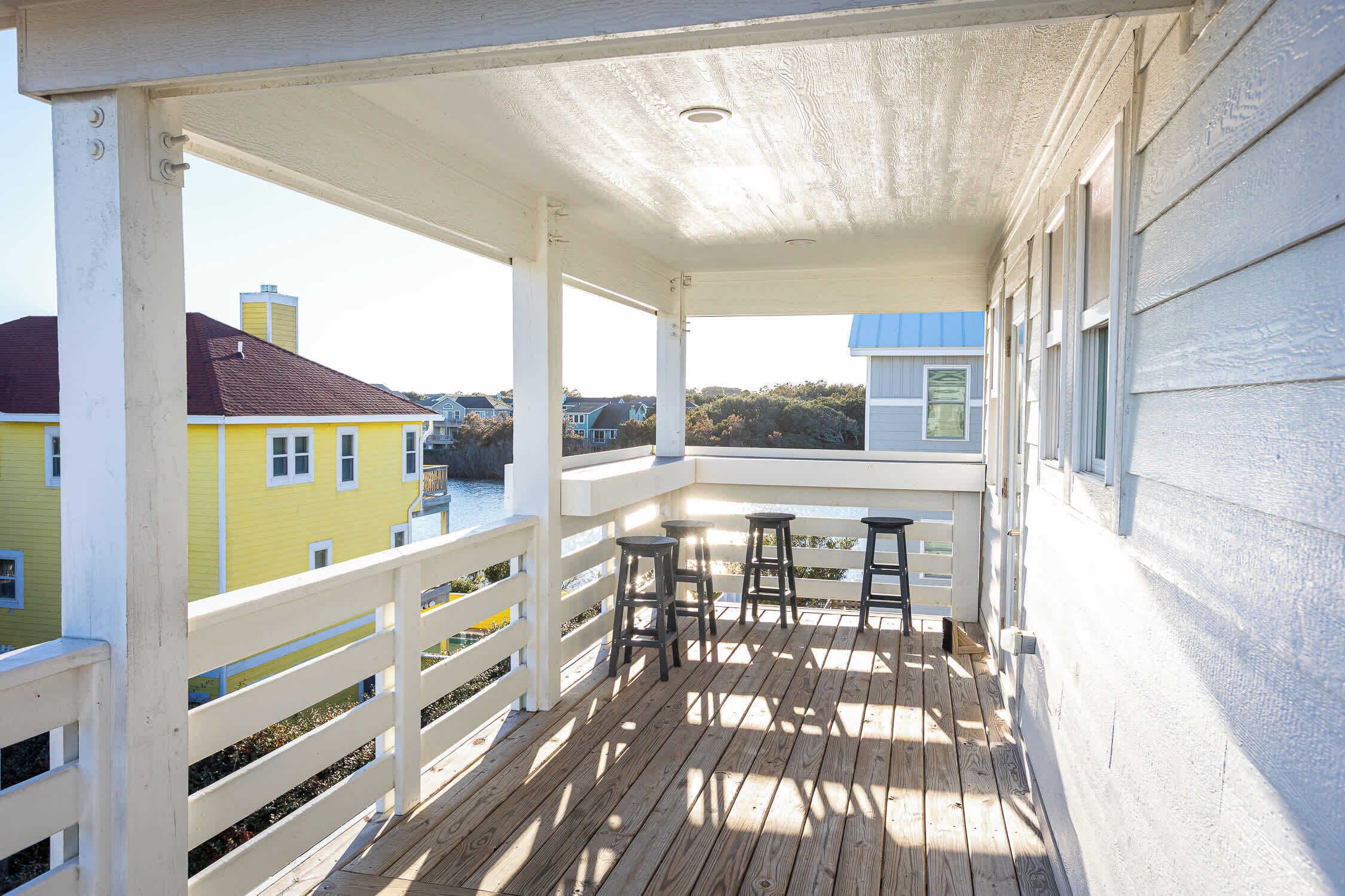 A wooden deck with white railings and three black stools.