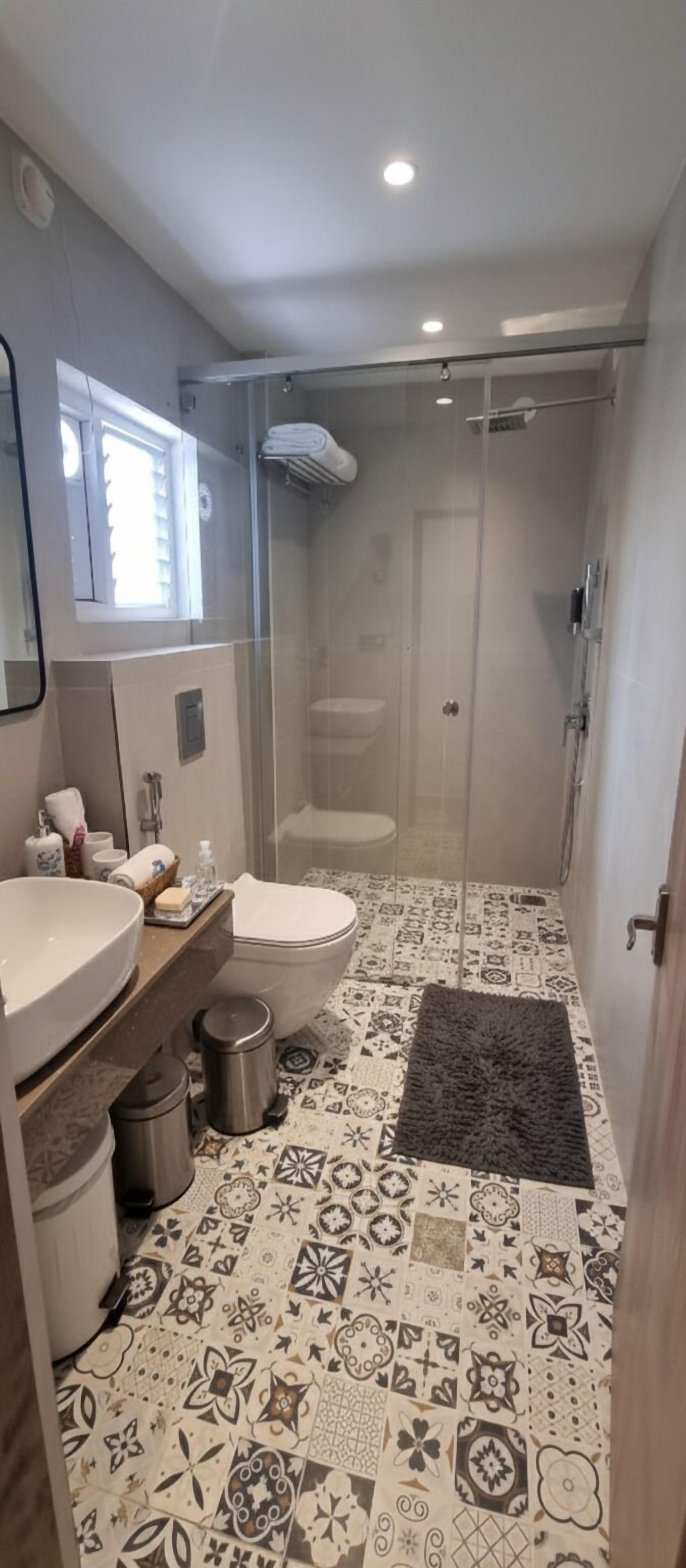 A modern bathroom with a glass-enclosed shower, a large sink, and patterned floor tiles.