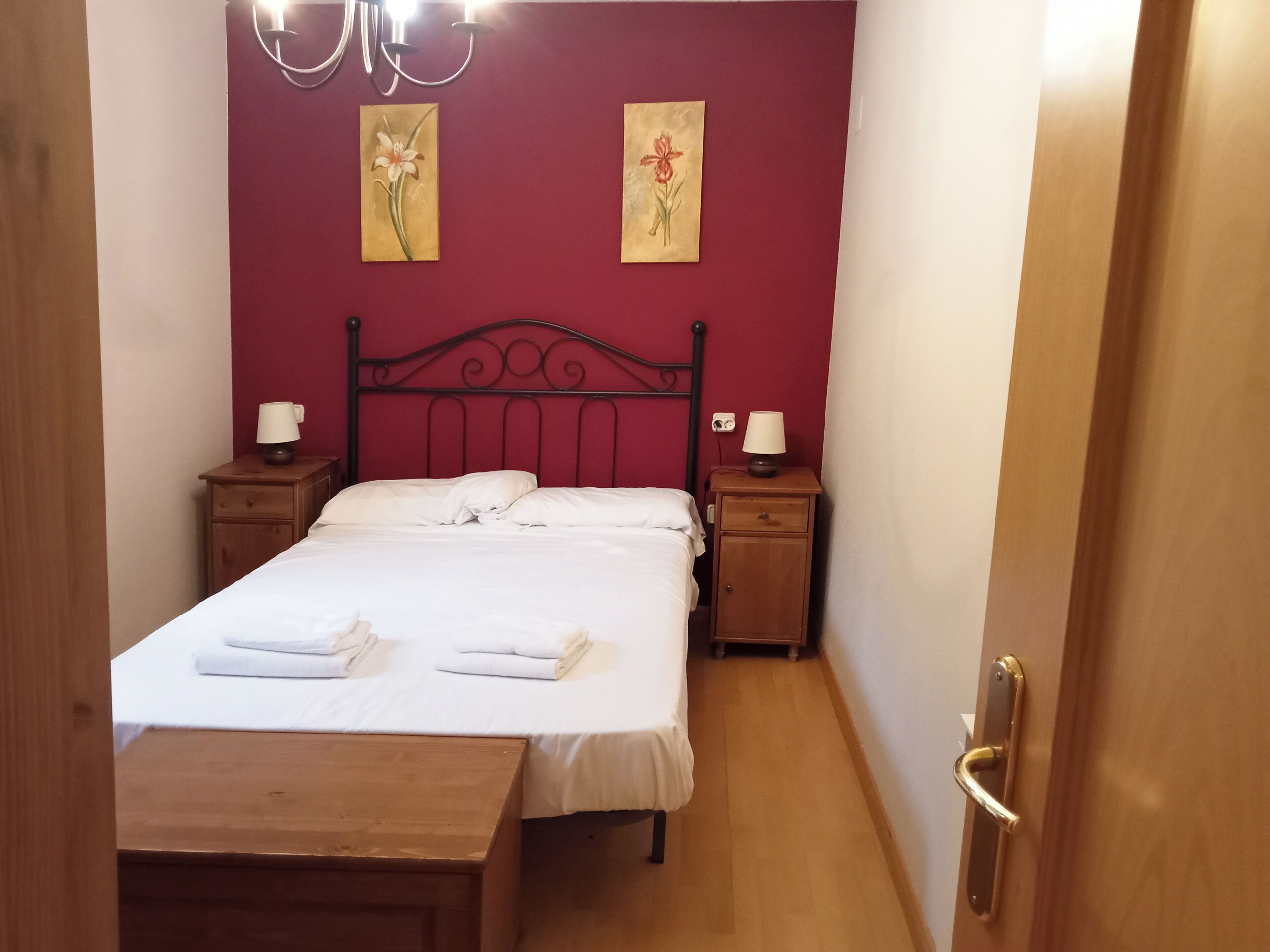 A bedroom with a bed, two nightstands, a wooden bench, and two wall-mounted lamps.