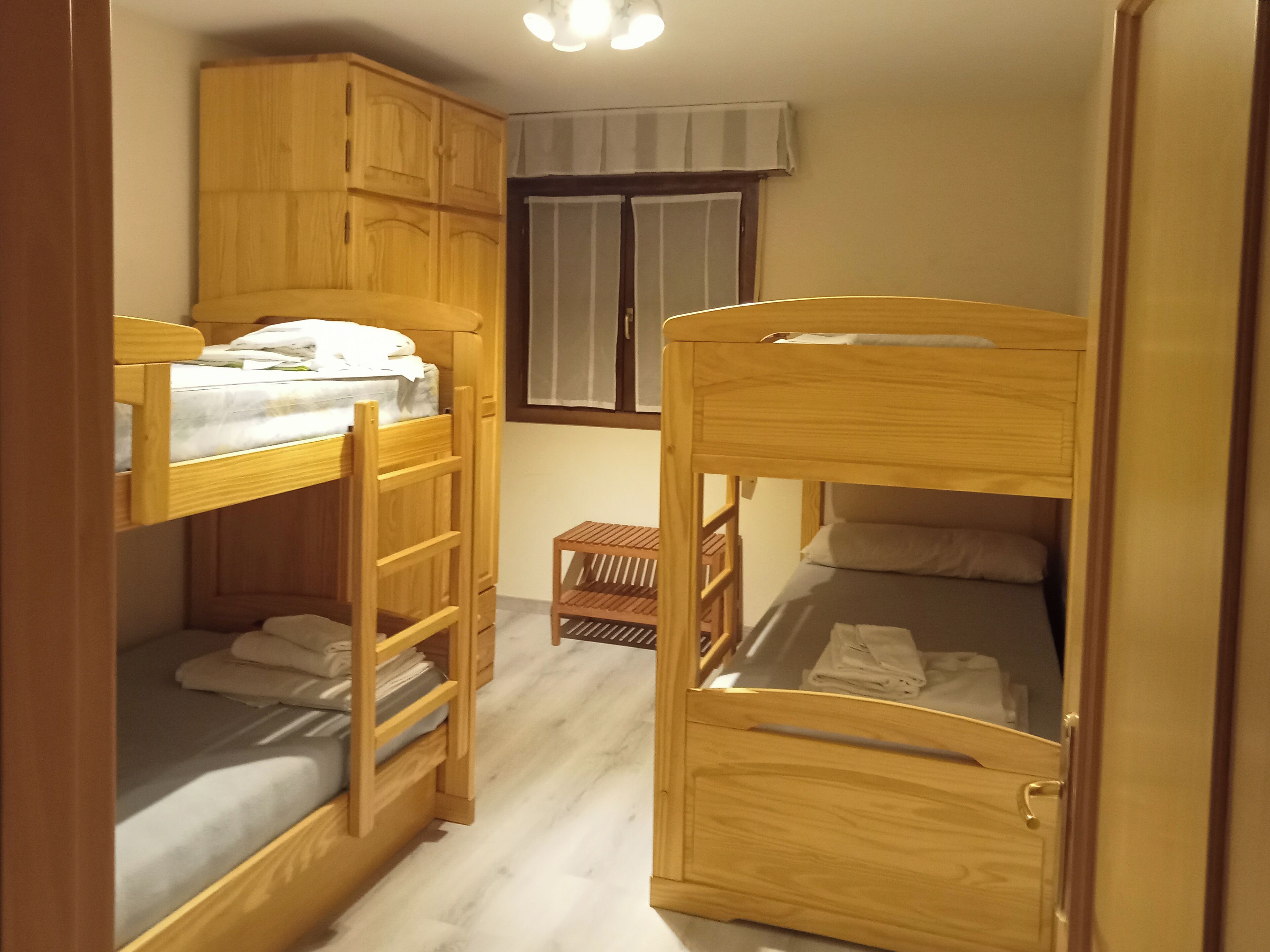 Een kleine kamer met twee stapelbedden, houten kasten, een tafeltje en een raam met gordijnen.