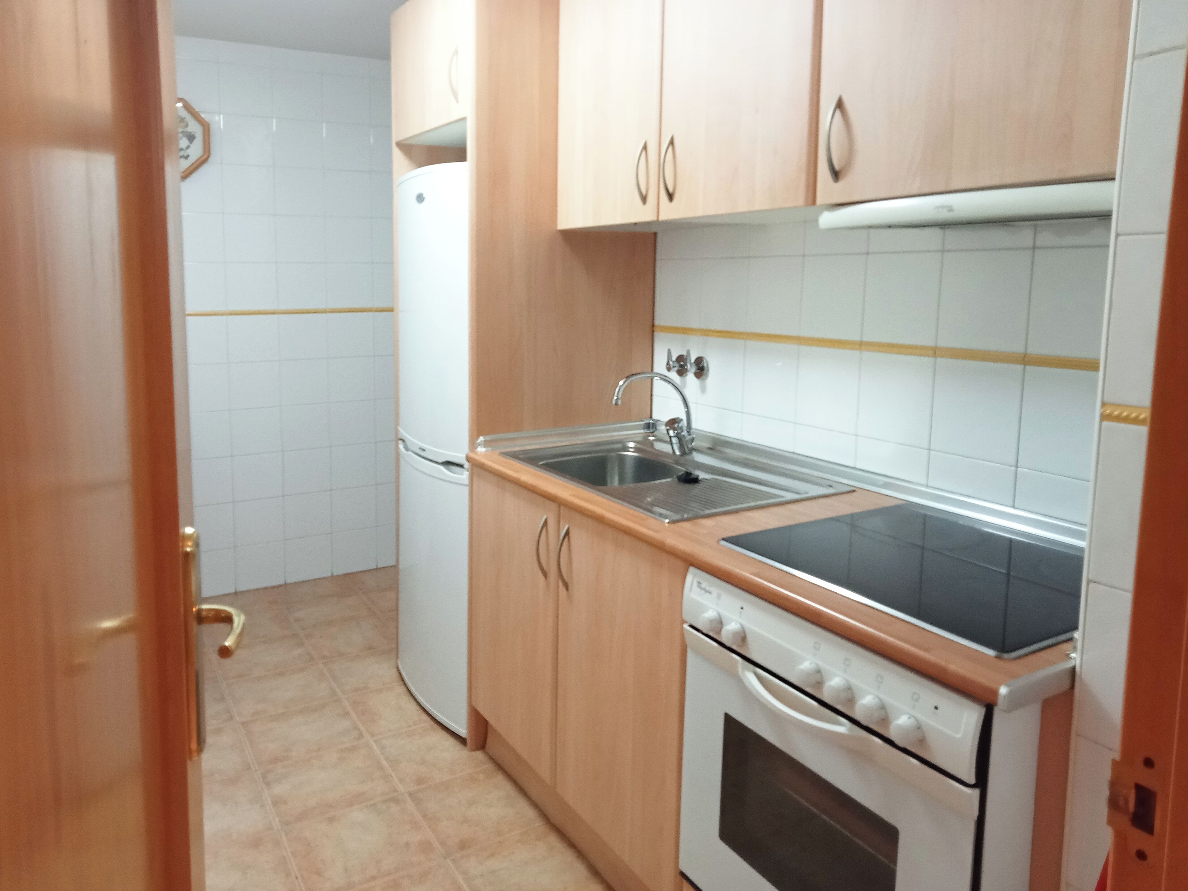A compact kitchen with wooden cabinets, a stainless steel sink, a built-in oven, and a white refrigerator.