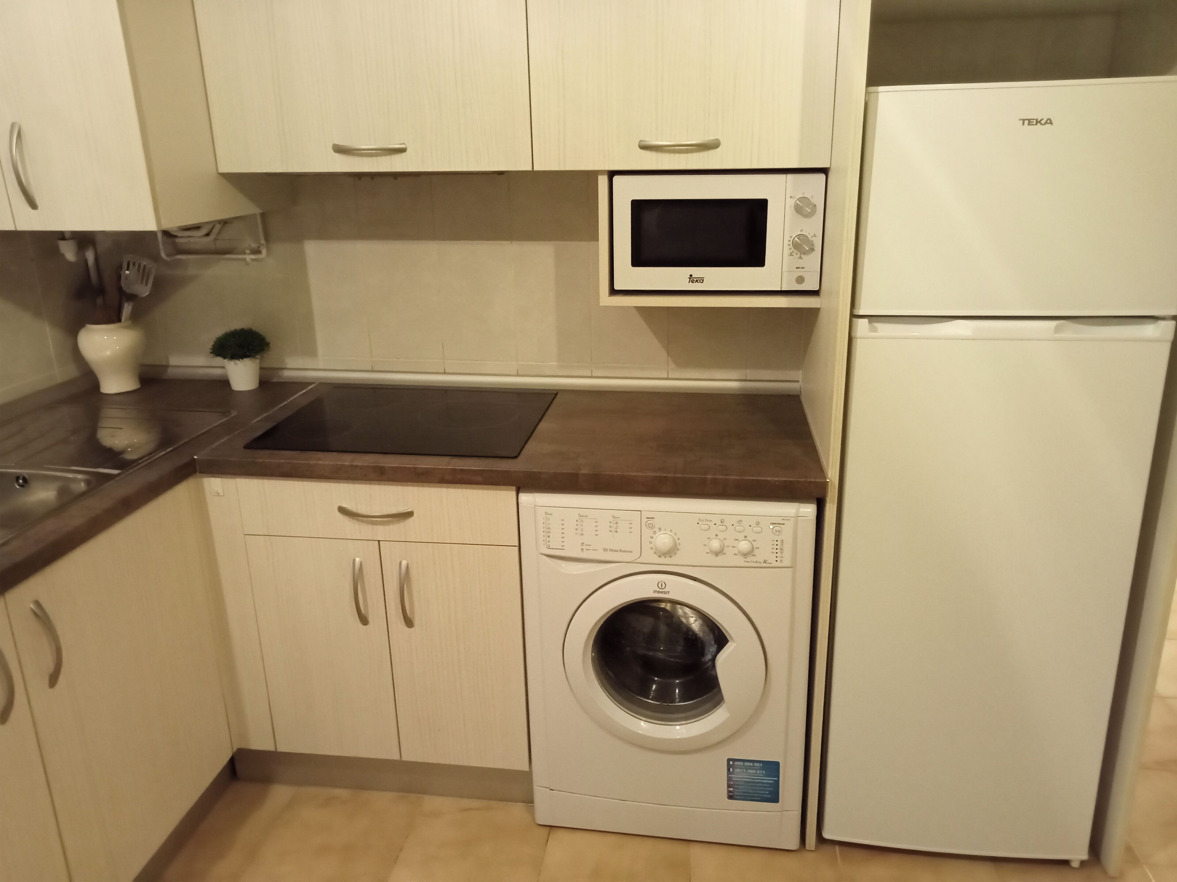 A compact kitchen with a microwave, a washing machine, and a refrigerator.