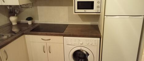 A compact kitchen with a microwave, a washing machine, and a refrigerator.