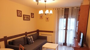 Un salon avec un canapé, une petite table et une chaise. Des tableaux encadrés ornent le mur, et il y a une fenêtre avec des rideaux.
