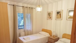 Une chambre avec deux lits, une fenêtre avec des rideaux, une table de chevet avec une lampe et des œuvres d’art encadrées accrochées au mur.