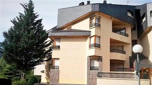 Un immeuble résidentiel à plusieurs étages, doté de balcons, d’un rez-de-chaussée en pierre et d’une façade de couleur claire.