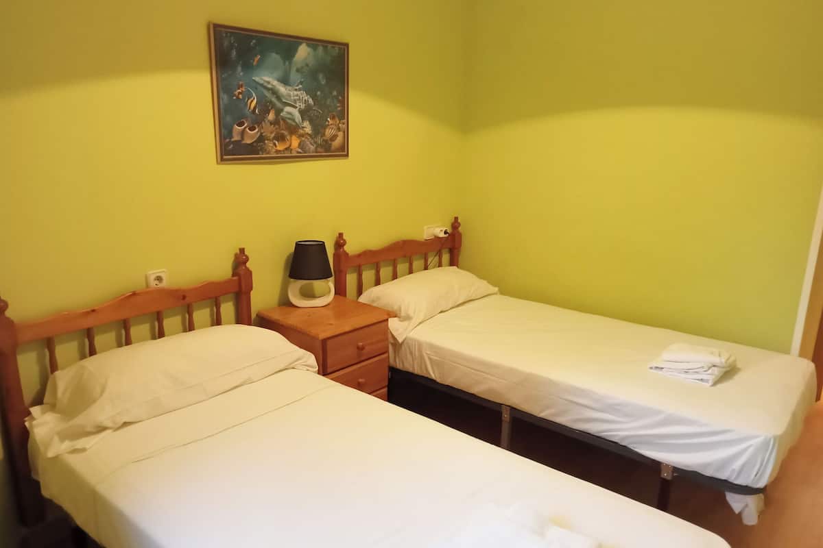 Una habitación con dos camas individuales, una mesita de noche con una lámpara y un cuadro en la pared.