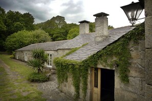 A stone building with a sloped roof, a wooden door, and a lantern on the right side. - Rural house, fireplace, large garden, close to hiking trails and spa. (Guitiriz)