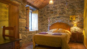 Un dormitorio con pared de piedra, una cama de madera, una mesita de noche, una silla y una ventana con cortina.