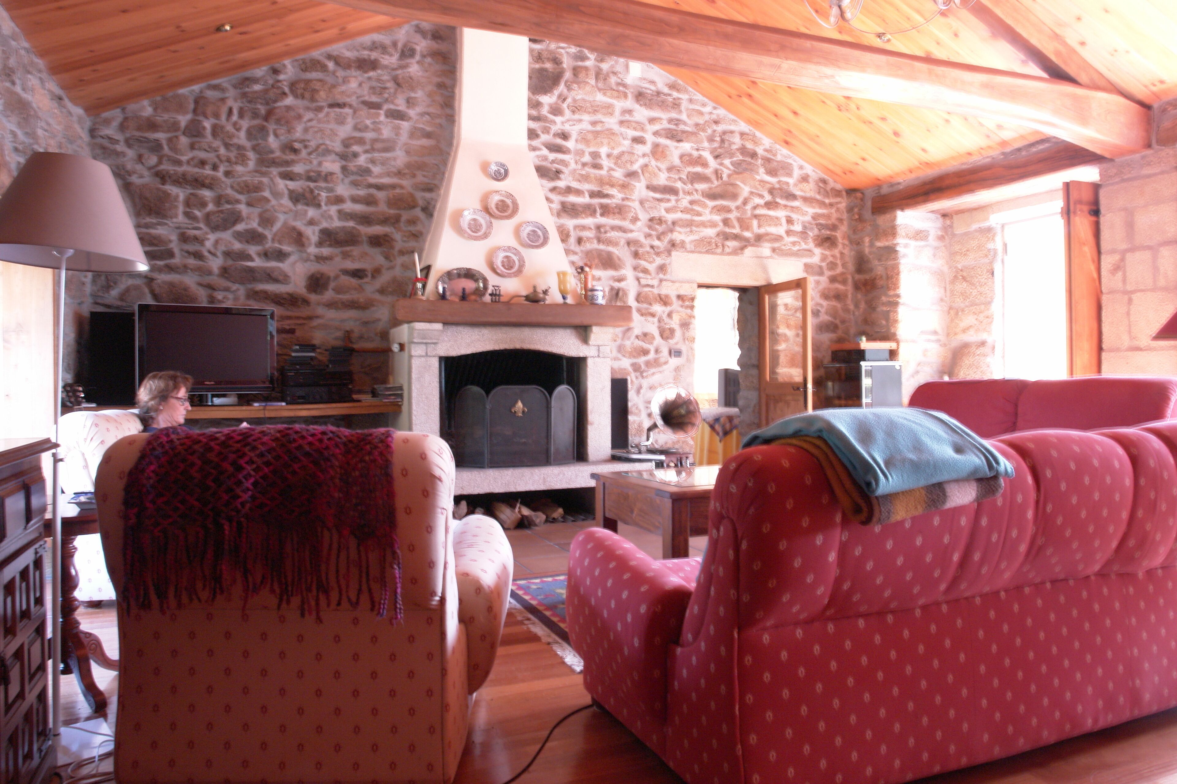 A cozy living room with a stone wall, a fireplace, a television, and a red sofa.