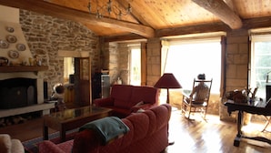 Una sala de estar acogedora con pared de piedra, vigas de madera en el techo, chimenea y sofá rojo.