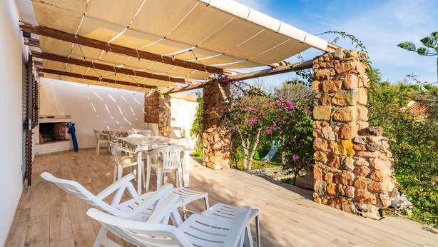 Une terrasse extérieure couverte, avec des murs en pierre, des chaises en plastique blanches et une table.